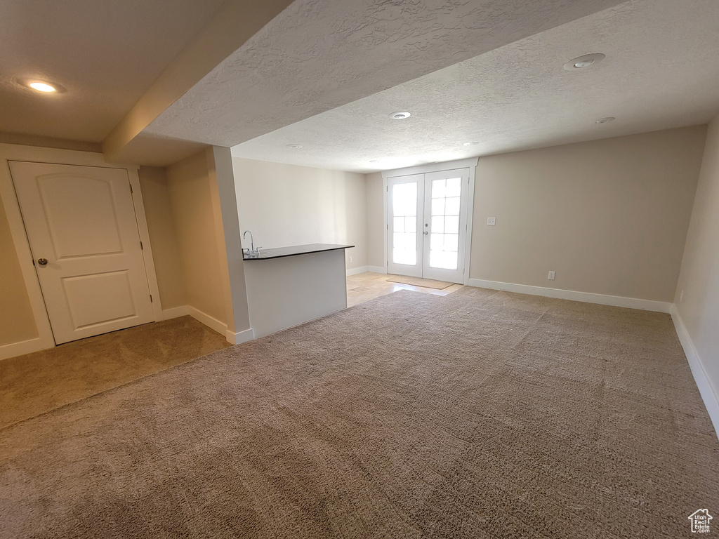 Below grade area with light carpet, baseboards, a textured ceiling, french doors, and recessed lighting