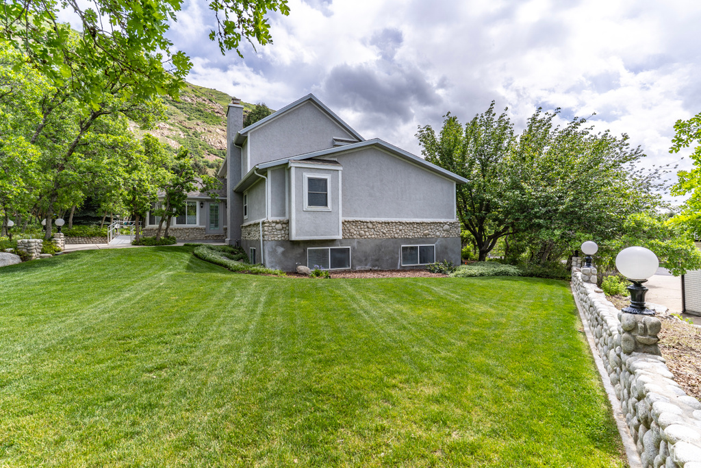 View of side of property with a chimney, a yard, stucco siding, and stone siding