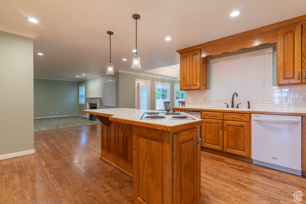 Kitchen featuring white appliances, a sink, ornamental molding, tile counters, and wood finished floors