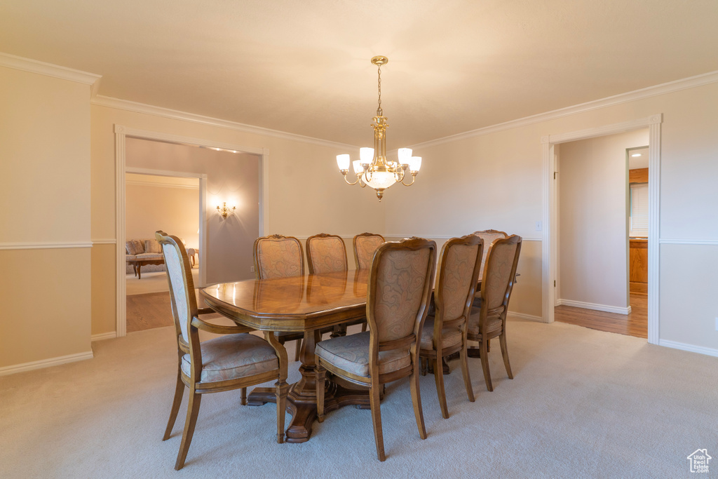 Dining area with a chandelier, light carpet, crown molding, and baseboards