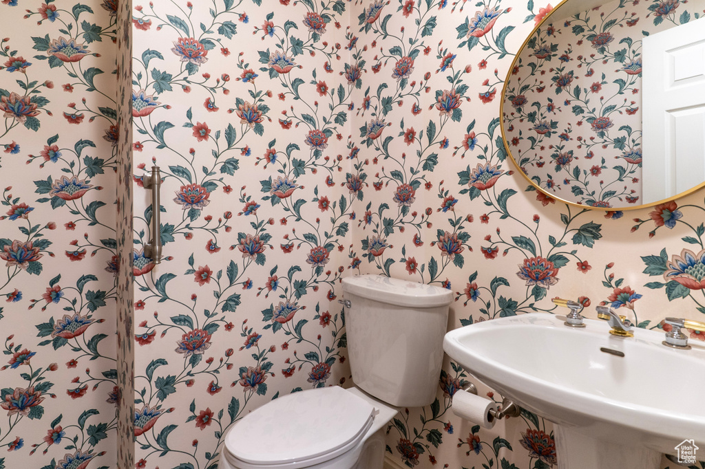 Bathroom featuring a sink, toilet, and wallpapered walls