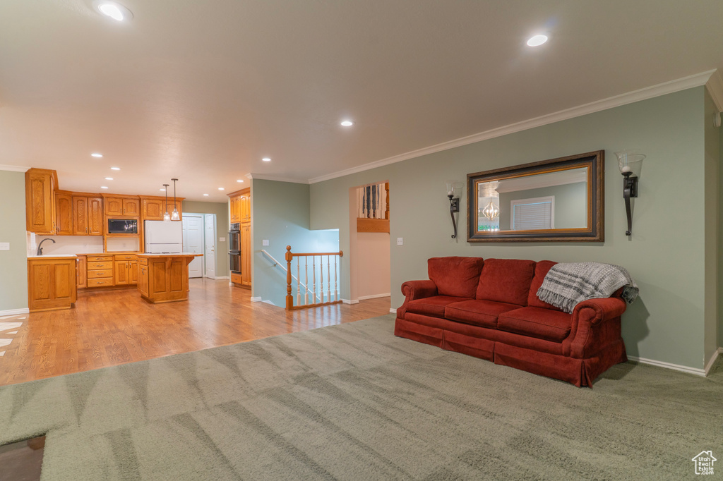 Living room with ornamental molding, baseboards, recessed lighting, light colored carpet, and light wood-type flooring