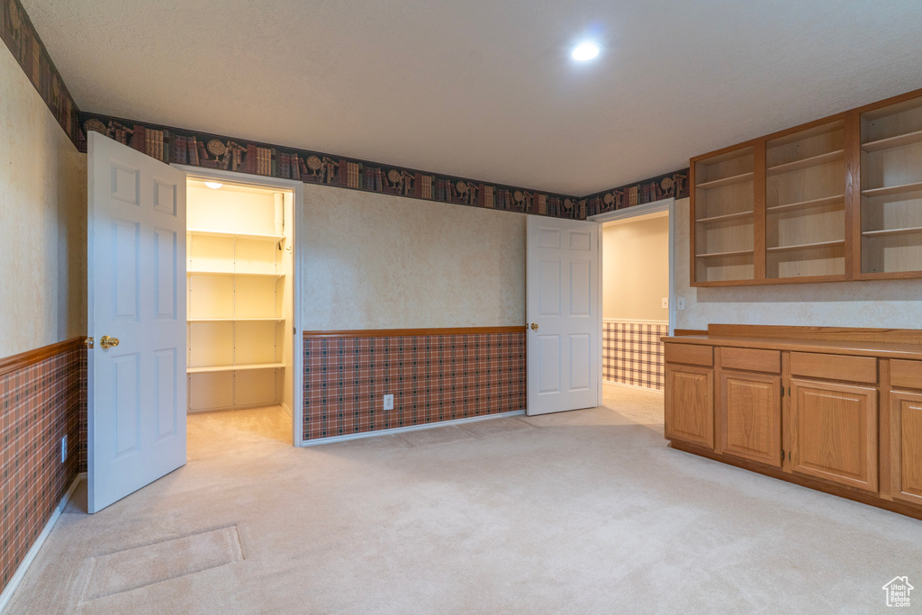 Unfurnished bedroom featuring a wainscoted wall, light carpet, and wallpapered walls