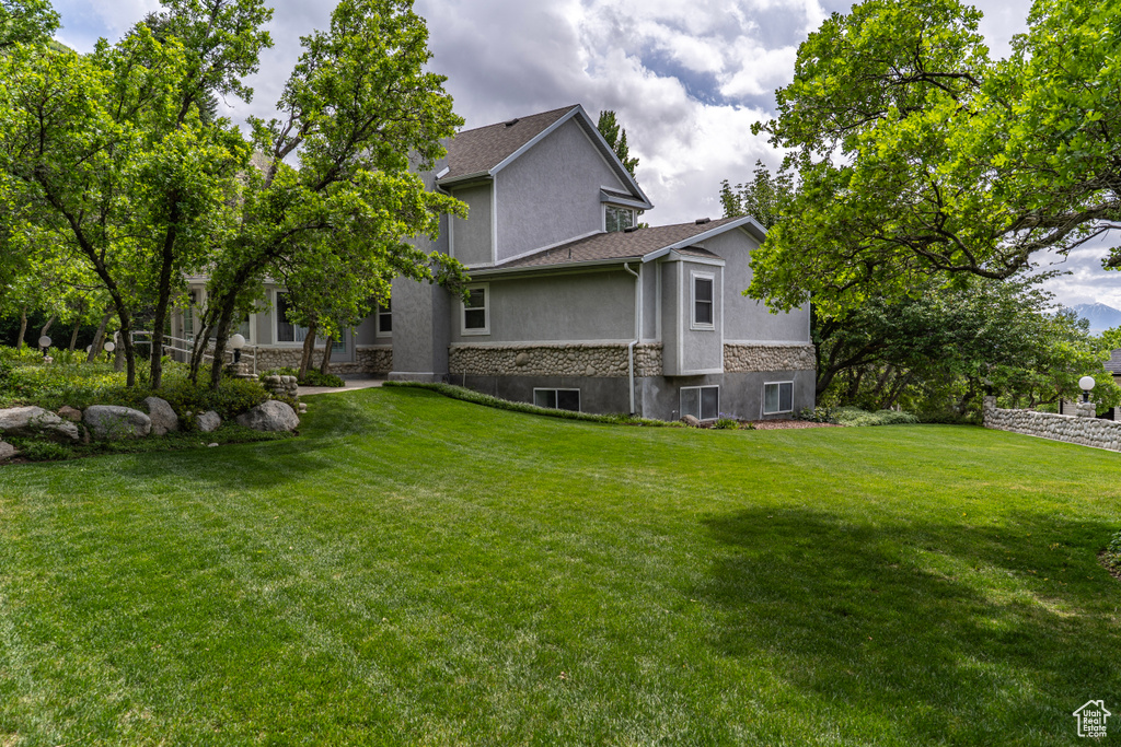 Rear view of property featuring stucco siding, stone siding, and a yard