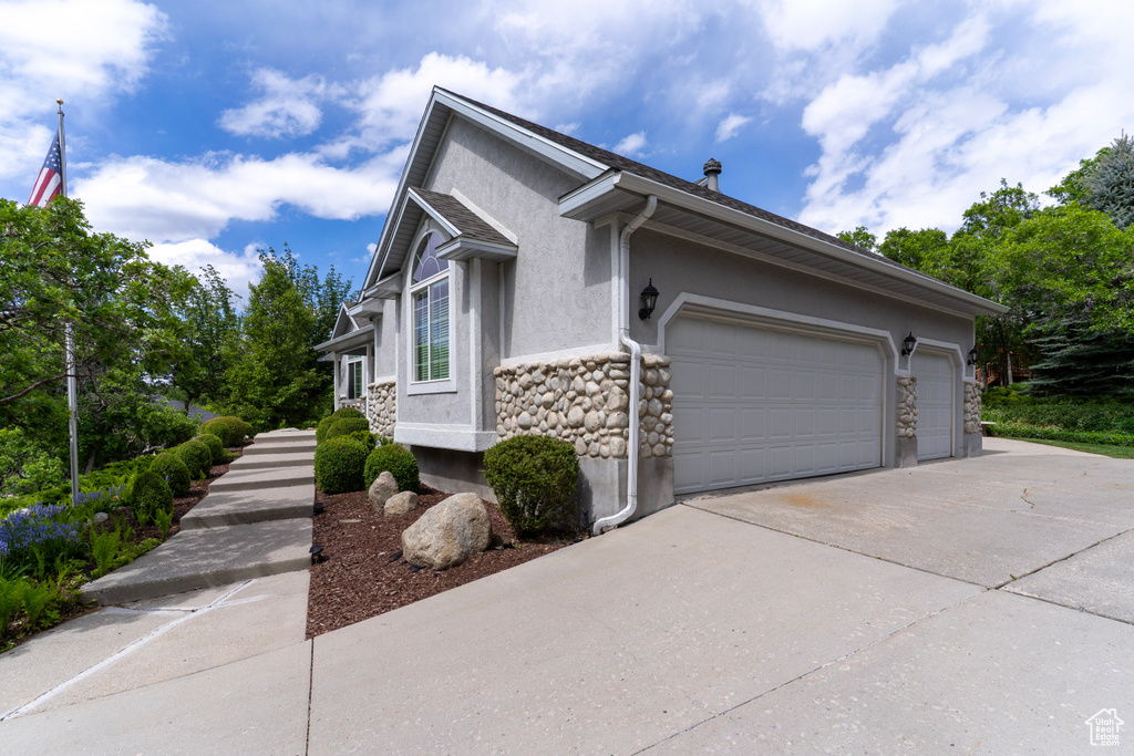 View of side of property with stucco siding, concrete driveway, stone siding, and an attached garage