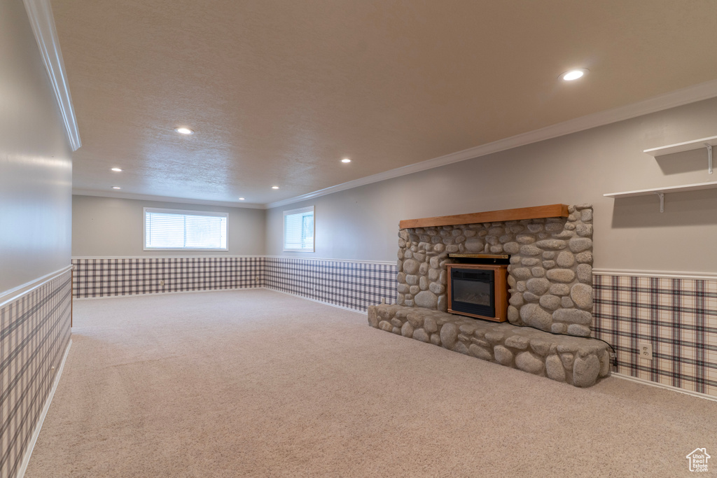 Unfurnished living room with ornamental molding, recessed lighting, wainscoting, a stone fireplace, and carpet flooring