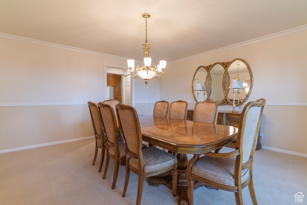 Dining space with a chandelier, light carpet, baseboards, and ornamental molding