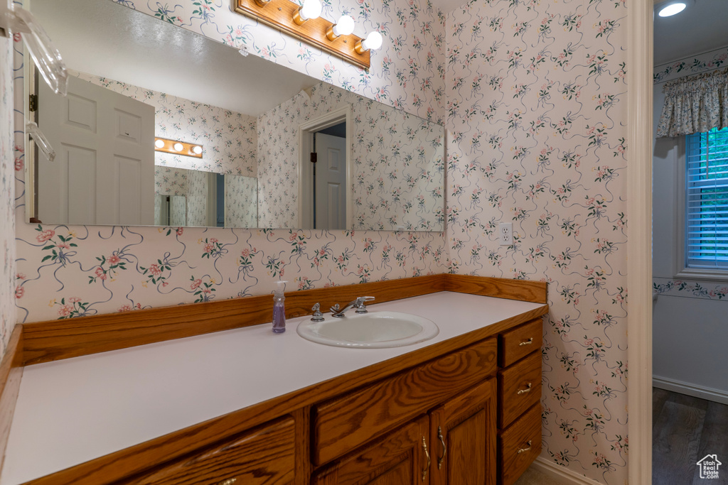 Bathroom featuring wallpapered walls, vanity, baseboards, and wood finished floors