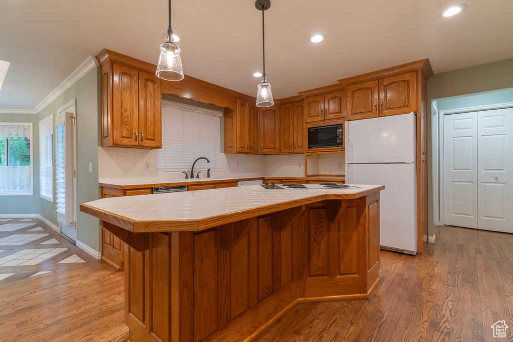 Kitchen with tile counters, white appliances, a kitchen island, ornamental molding, and brown cabinetry