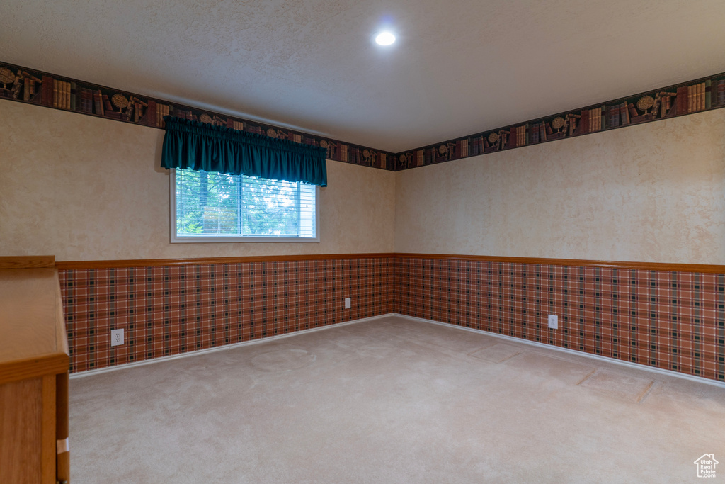 Carpeted empty room featuring a wainscoted wall and wallpapered walls