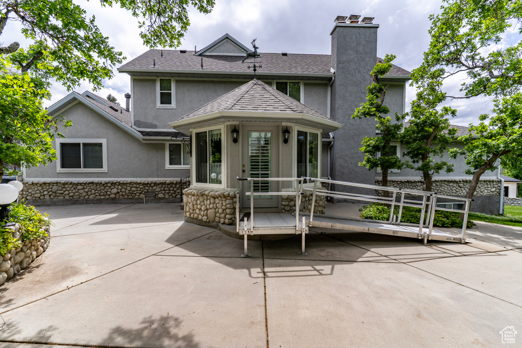 Back of house featuring stucco siding, a chimney, a patio, stone siding, and a shingled roof