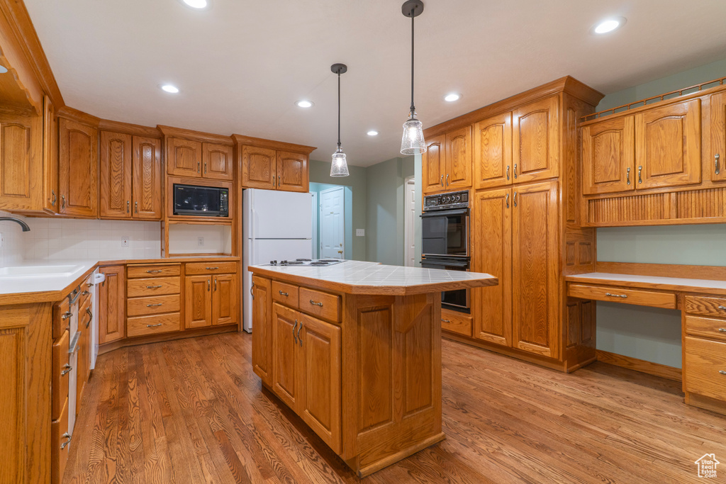 Kitchen with black appliances, a sink, tile countertops, light wood finished floors, and recessed lighting