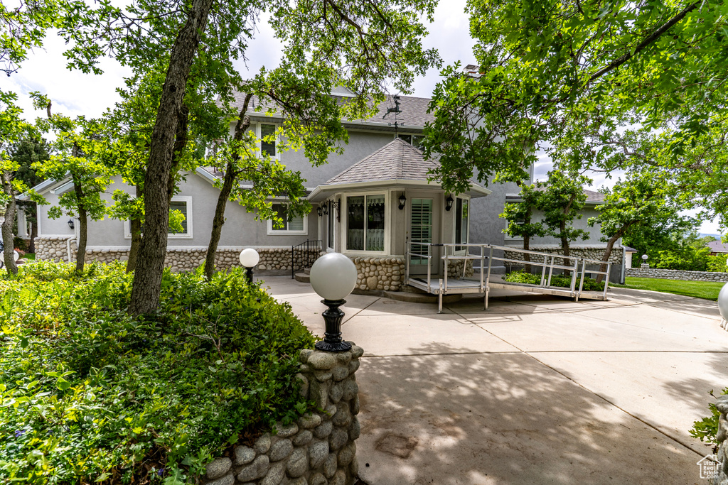 View of front facade featuring stucco siding, stone siding, a shingled roof, and a patio area