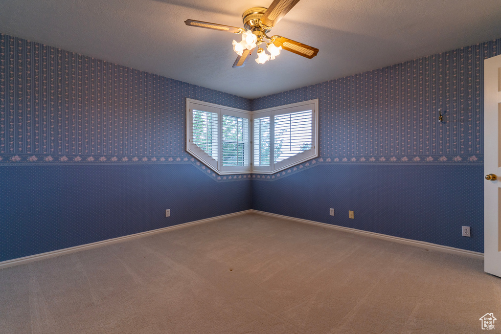 Carpeted empty room featuring wallpapered walls, ceiling fan, and baseboards