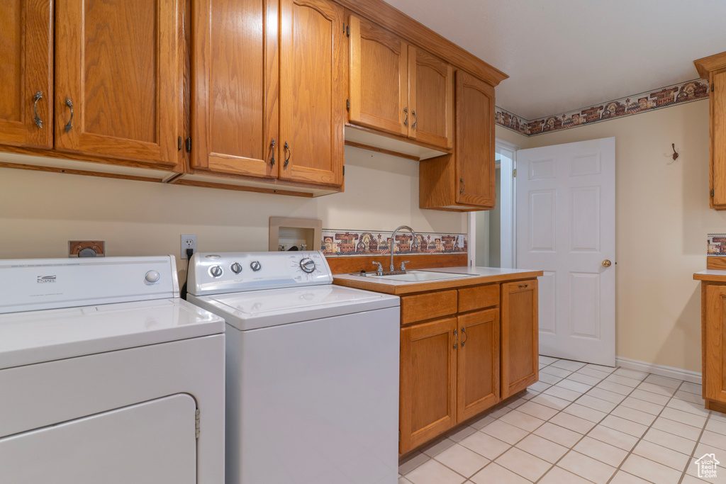 Clothes washing area with washer and clothes dryer, cabinet space, light tile patterned floors, and baseboards