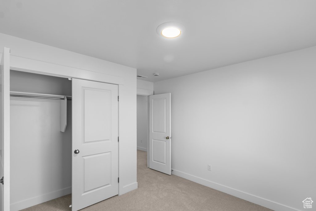 Unfurnished bedroom featuring light carpet, baseboards, and a closet
