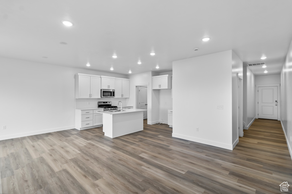 Kitchen with appliances with stainless steel finishes, recessed lighting, a center island with sink, a sink, and white cabinets