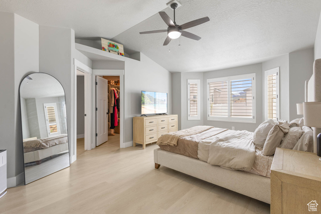Bedroom with light wood-style floors, a walk in closet, vaulted ceiling, ceiling fan, and a closet
