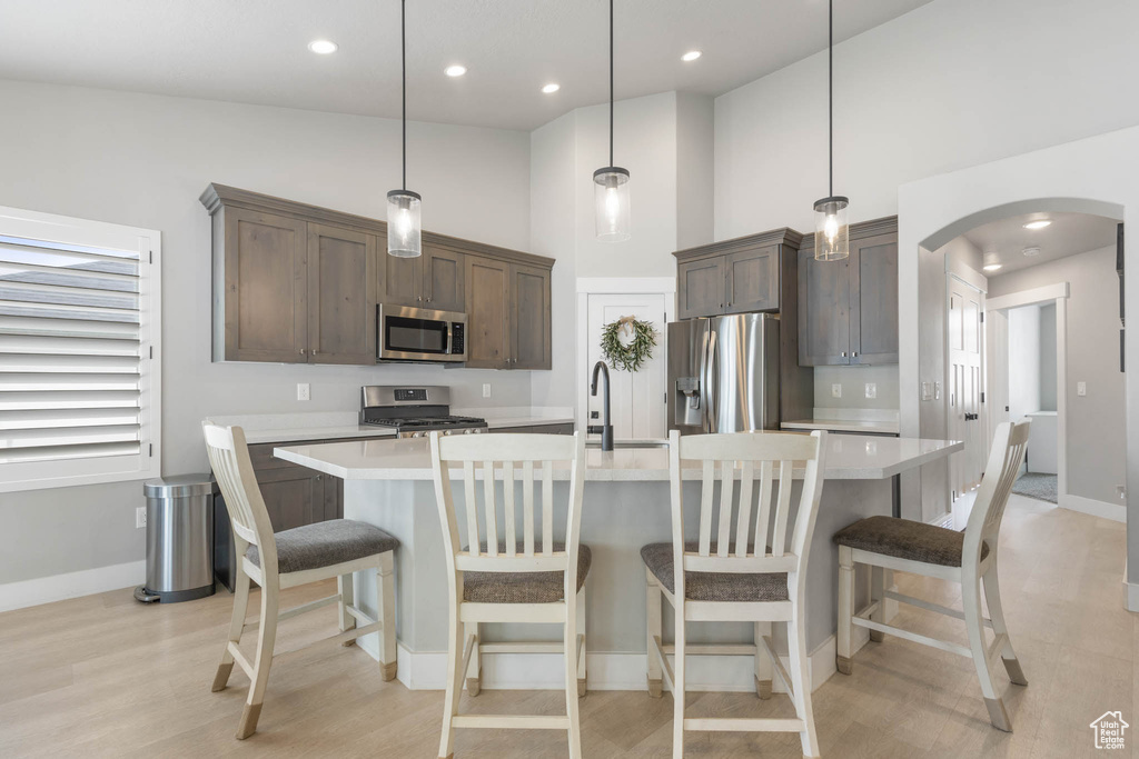 Kitchen featuring stainless steel appliances, arched walkways, light countertops, a kitchen island with sink, and hanging light fixtures
