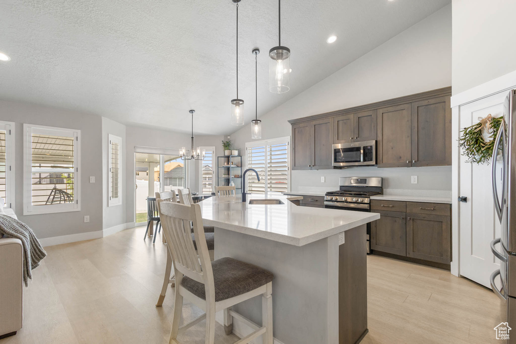 Kitchen featuring a sink, stainless steel appliances, light wood-style floors, light countertops, and a kitchen breakfast bar