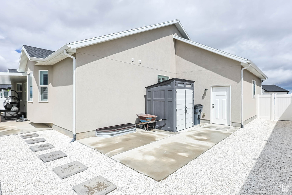 Rear view of property featuring a storage unit, a patio, an outdoor structure, stucco siding, and fence