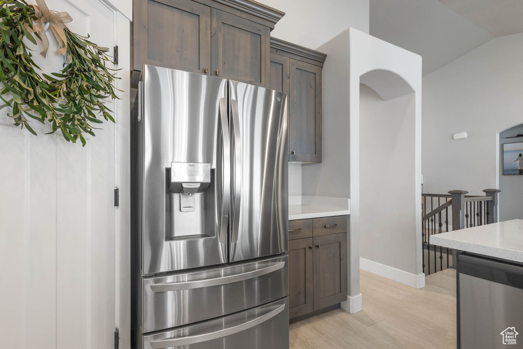 Kitchen featuring appliances with stainless steel finishes, light wood finished floors, dark brown cabinets, baseboards, and lofted ceiling