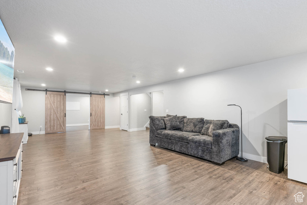 Living room with a barn door, light wood-type flooring, recessed lighting, and baseboards