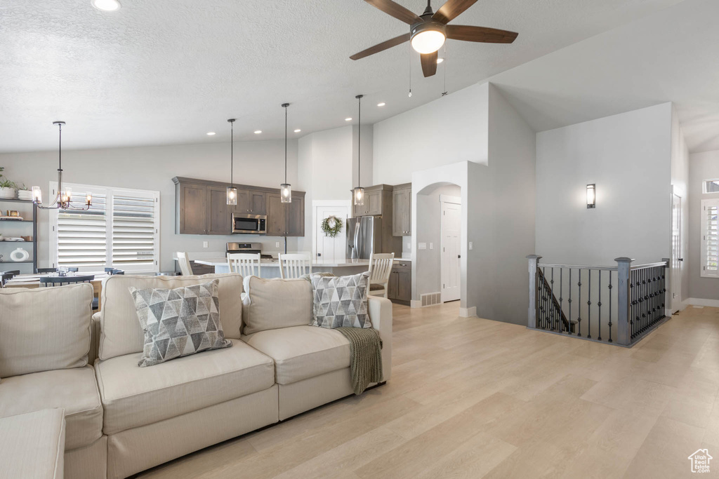 Living room featuring ceiling fan, light wood-style floors, arched walkways, recessed lighting, and a chandelier