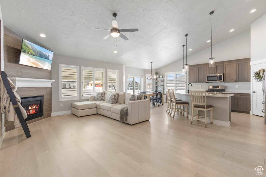 Living room featuring a textured ceiling, a ceiling fan, a tiled fireplace, lofted ceiling, and recessed lighting