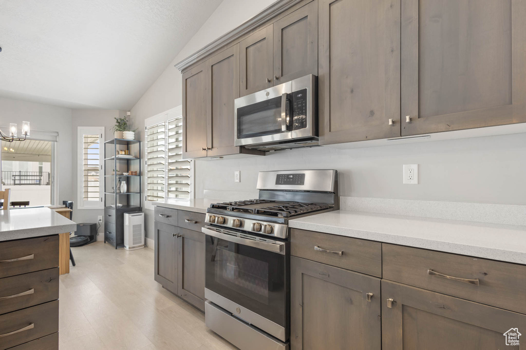 Kitchen with stainless steel appliances, light countertops, a chandelier, light wood-type flooring, and dark brown cabinets