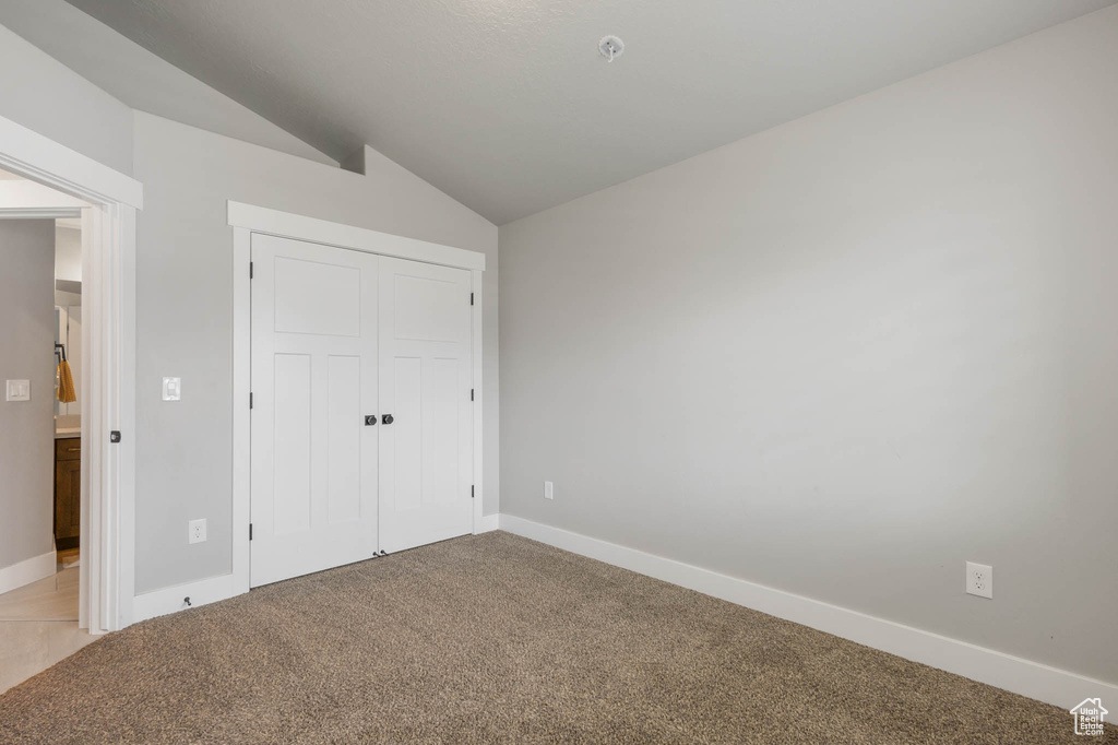 Unfurnished bedroom with vaulted ceiling, light carpet, baseboards, and a closet