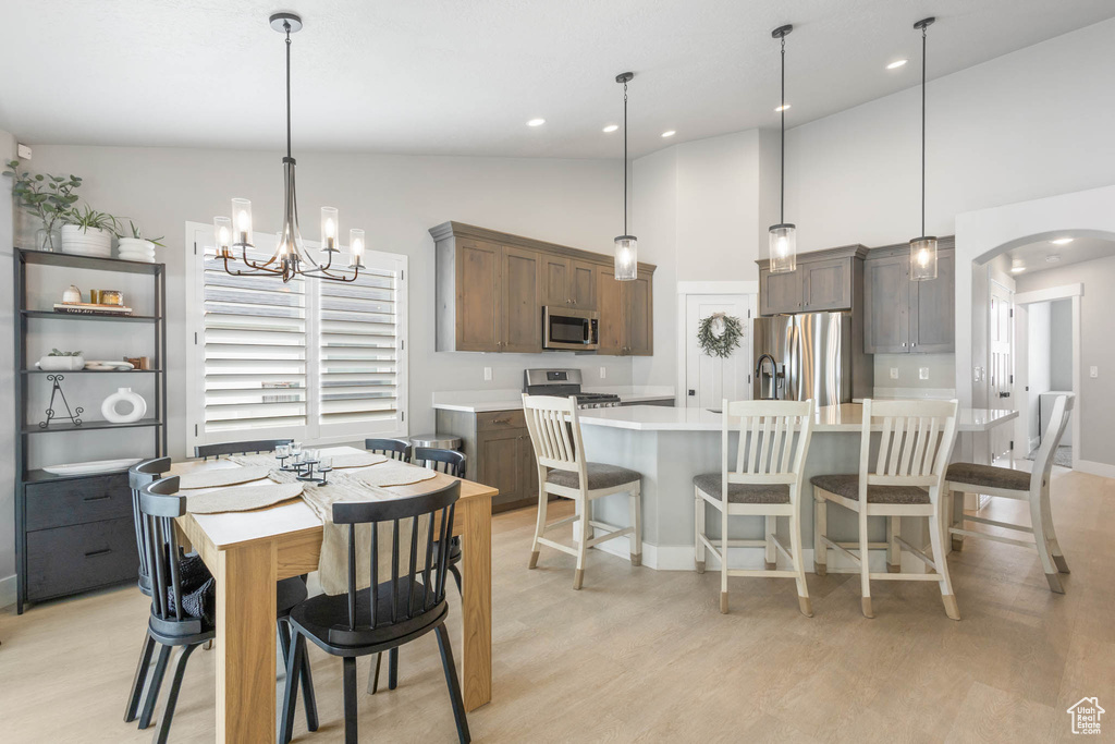 Dining area with light wood-type flooring, arched walkways, a chandelier, baseboards, and high vaulted ceiling