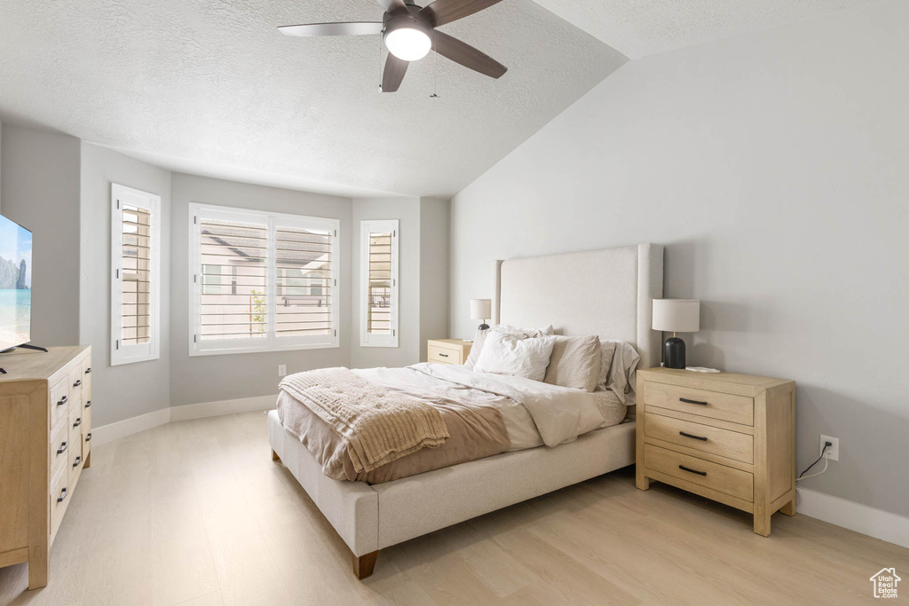 Bedroom with a textured ceiling, light wood finished floors, vaulted ceiling, baseboards, and ceiling fan