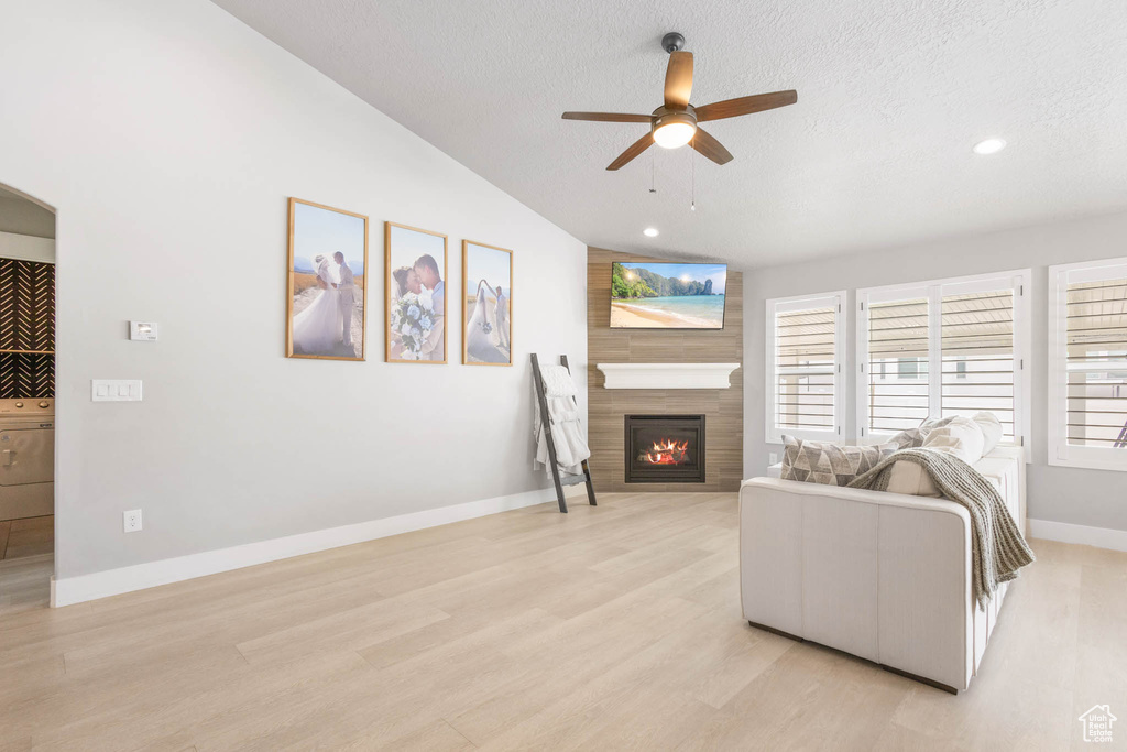Living room with ceiling fan, a fireplace, lofted ceiling, light wood finished floors, and a textured ceiling