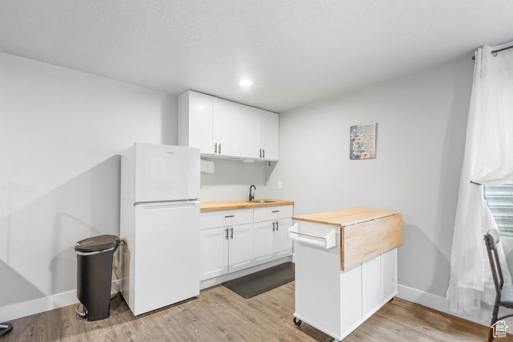 Kitchen featuring wood counters, freestanding refrigerator, a sink, and white cabinetry