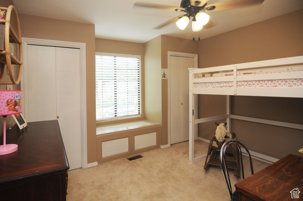 Bedroom with light colored carpet, two closets, and ceiling fan