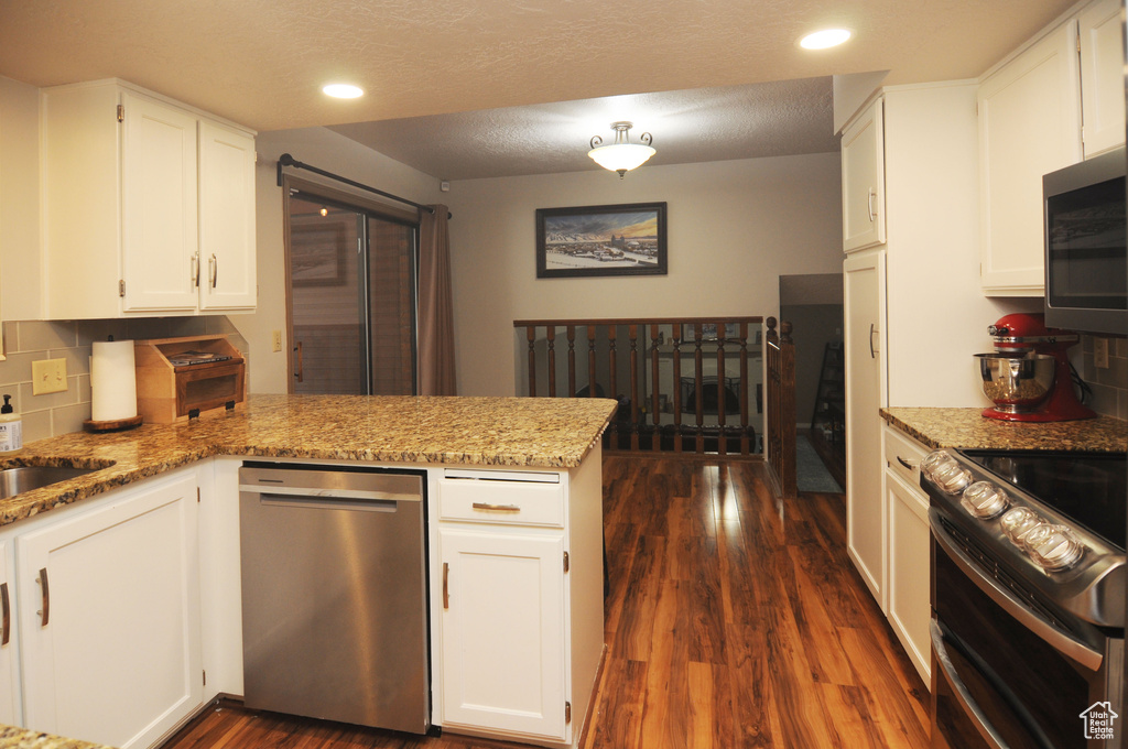 Kitchen with appliances with stainless steel finishes, a peninsula, dark wood-type flooring, tasteful backsplash, and white cabinets