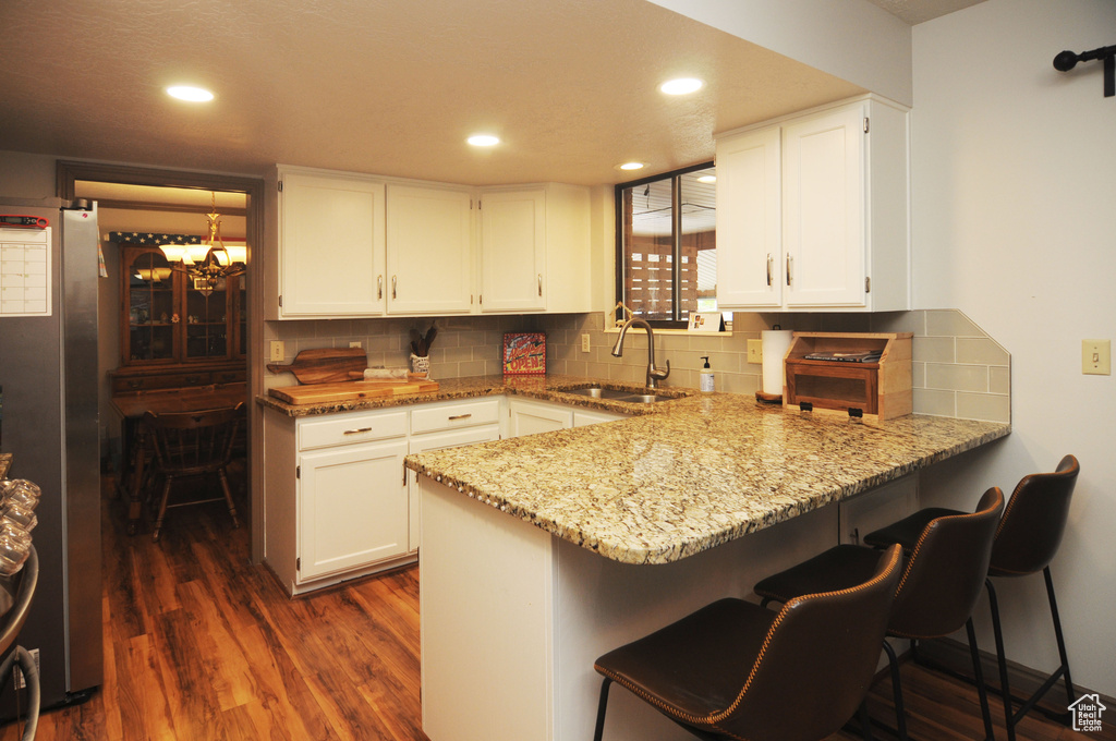 Kitchen with a sink, a peninsula, dark wood-style flooring, light stone countertops, and decorative backsplash