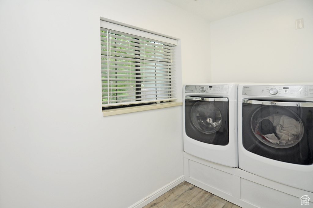 Clothes washing area with separate washer and dryer, light wood-style flooring, and baseboards