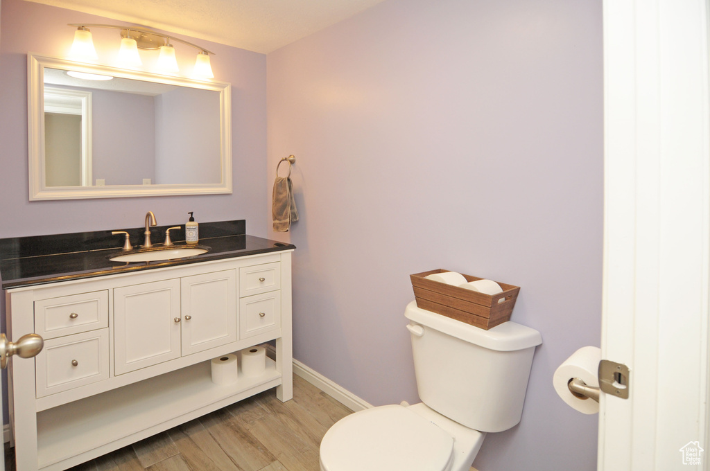 Half bath with wood finished floors, toilet, baseboards, and vanity