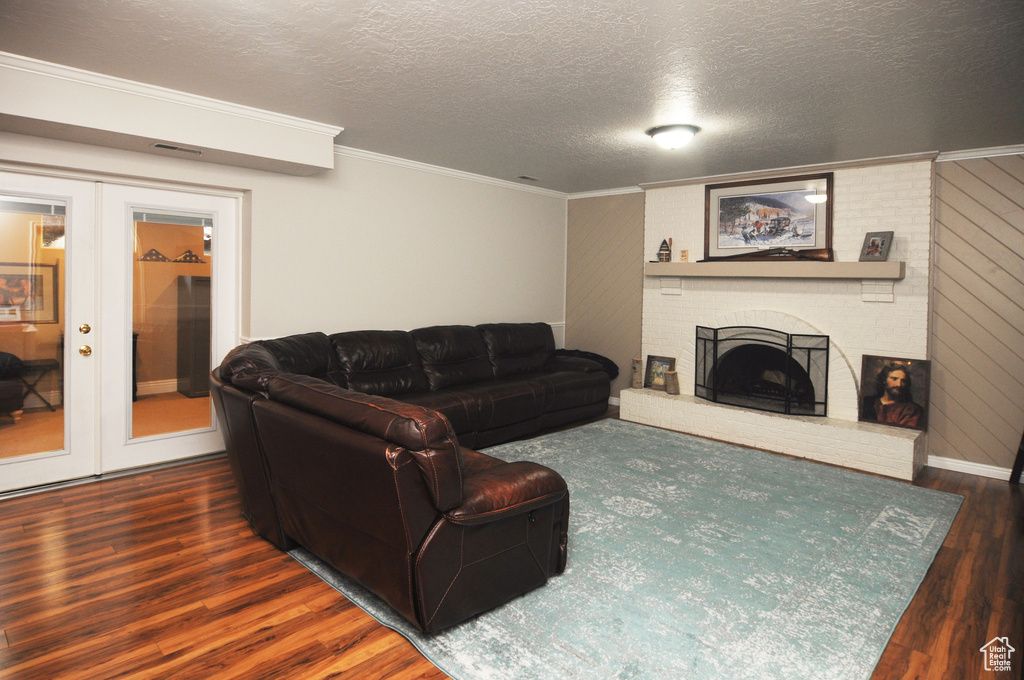 Living area with french doors, wood finished floors, crown molding, a fireplace, and a textured ceiling