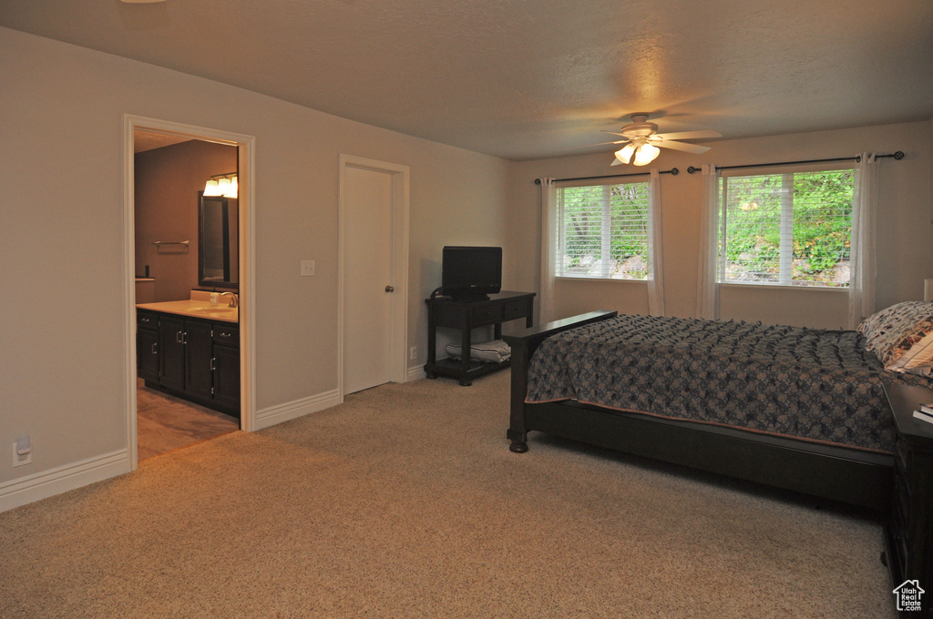 Bedroom featuring a sink, light colored carpet, baseboards, ensuite bath, and ceiling fan