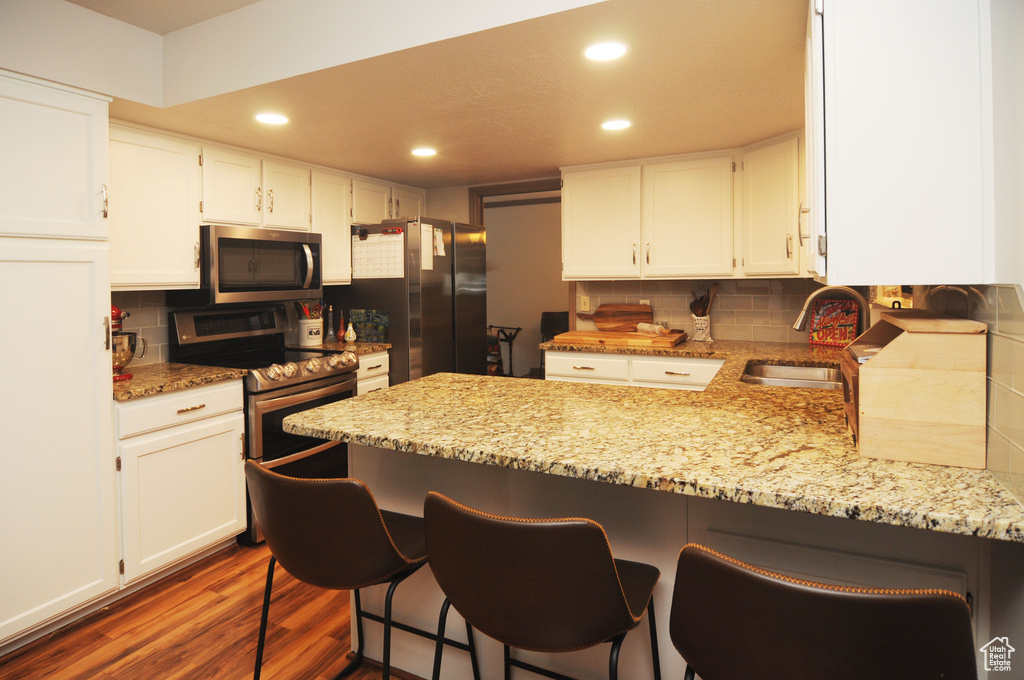Kitchen with appliances with stainless steel finishes, a sink, a peninsula, white cabinetry, and dark wood finished floors