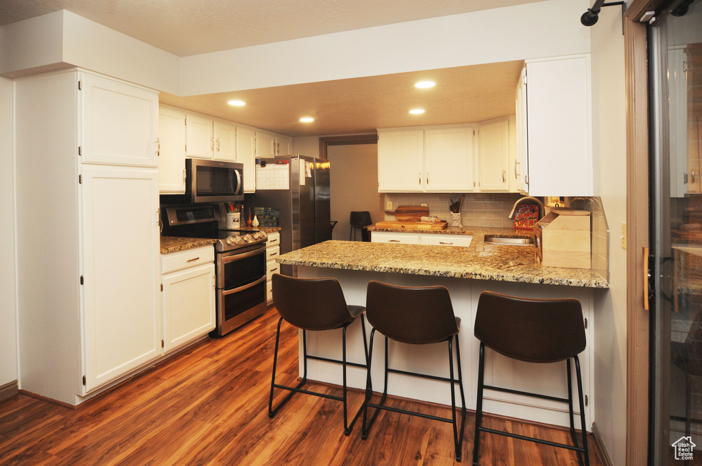 Kitchen with appliances with stainless steel finishes, a peninsula, tasteful backsplash, light stone countertops, and recessed lighting
