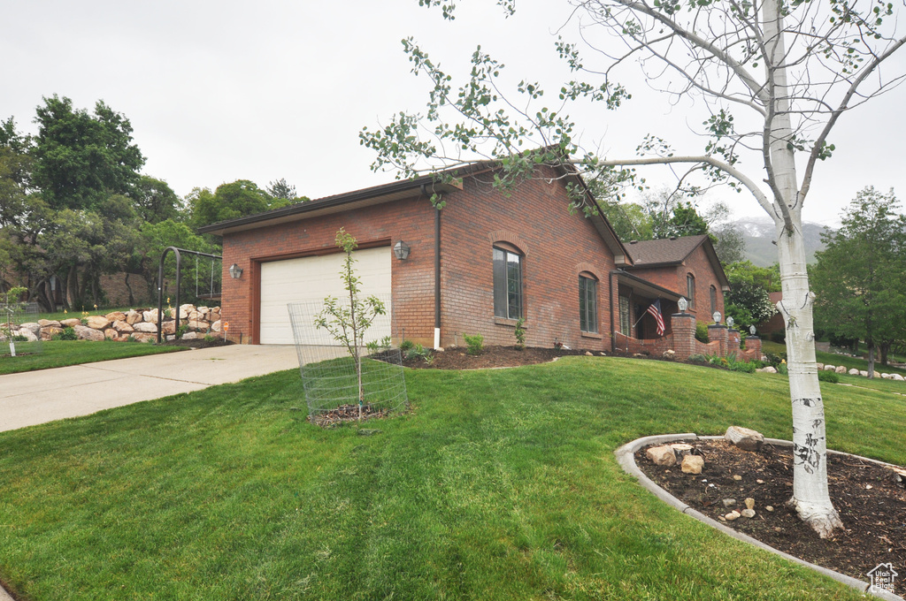 View of front of home with brick siding, driveway, an attached garage, and a front lawn