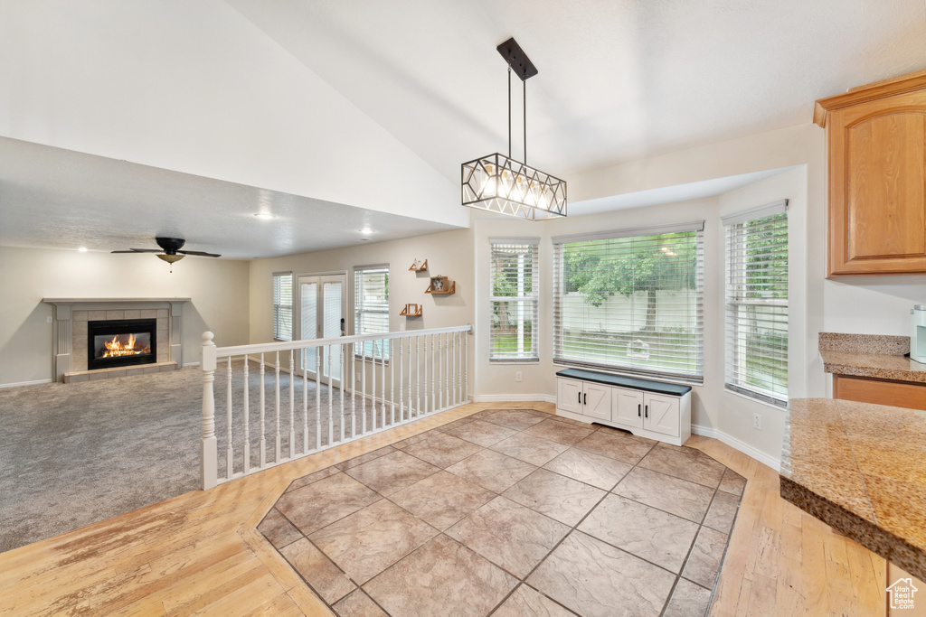 Unfurnished dining area with light wood finished floors, a ceiling fan, plenty of natural light, a fireplace, and high vaulted ceiling
