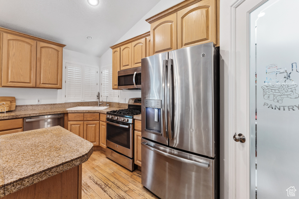 Kitchen with appliances with stainless steel finishes, a sink, vaulted ceiling, light wood finished floors, and recessed lighting
