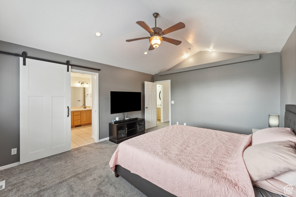Bedroom with a barn door, lofted ceiling, light colored carpet, ensuite bath, and baseboards