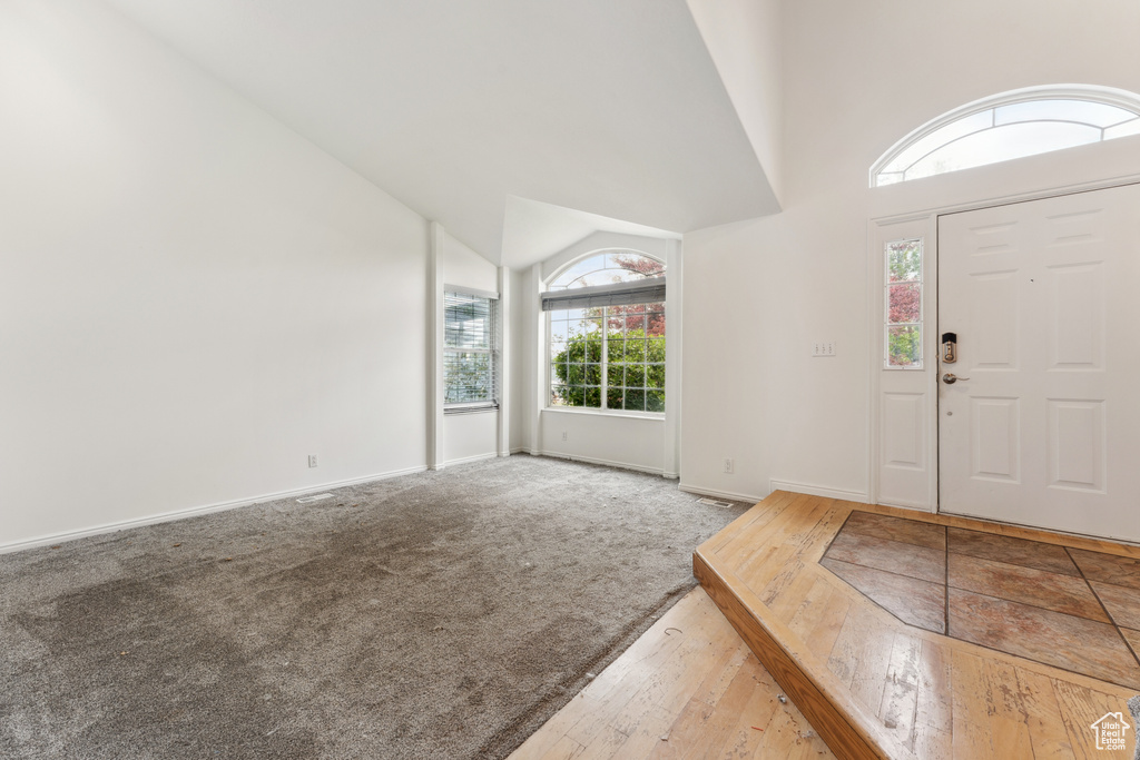 Carpeted foyer with hardwood / wood-style flooring, baseboards, and high vaulted ceiling