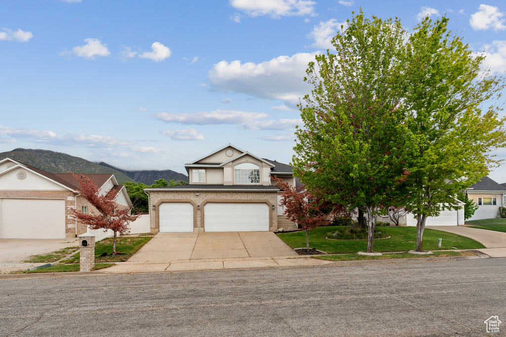 View of front facade with concrete driveway, a front lawn, a mountain view, brick siding, and a garage